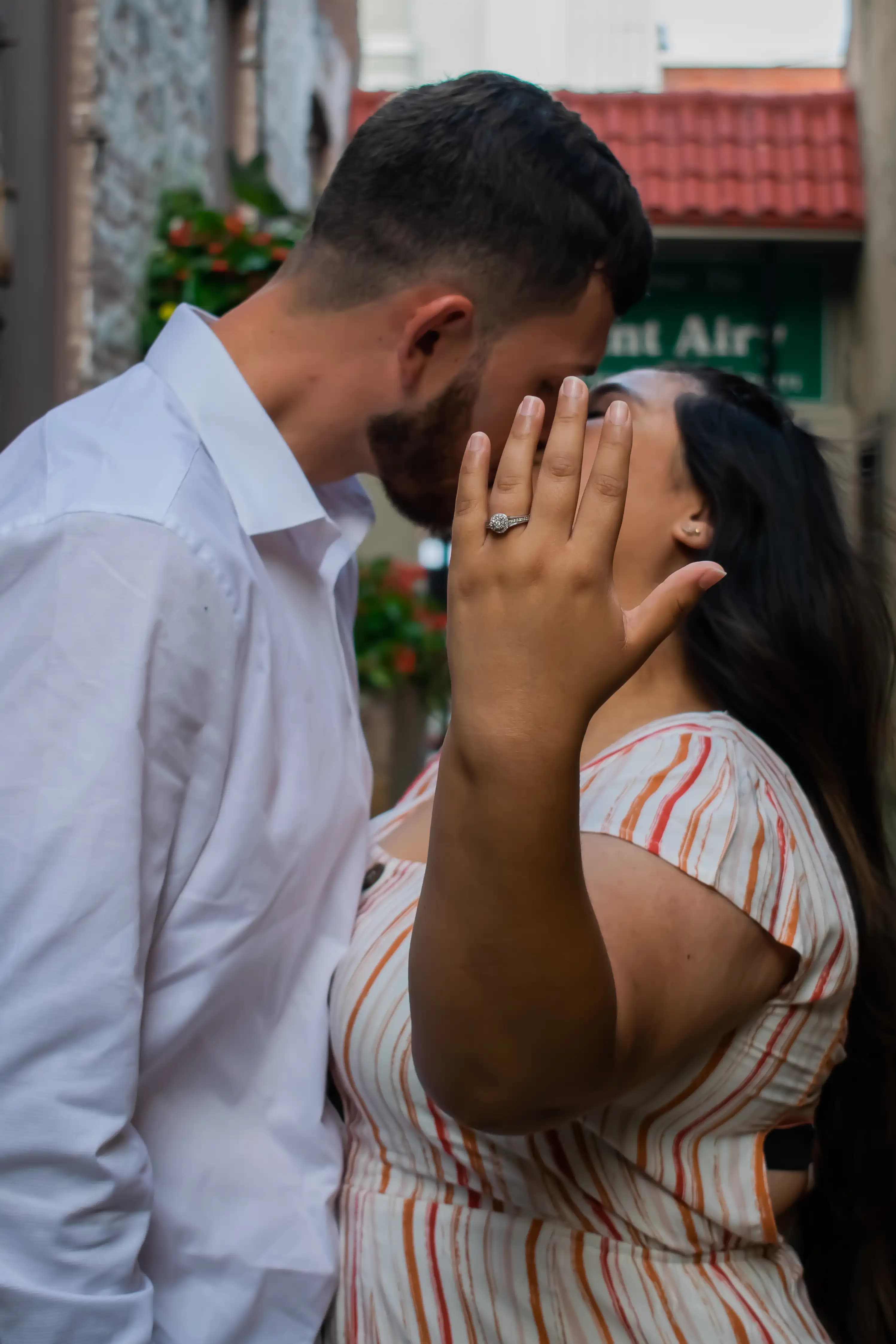 D + L kissing With the bride covering their faces holding her hand up showing off the ring.