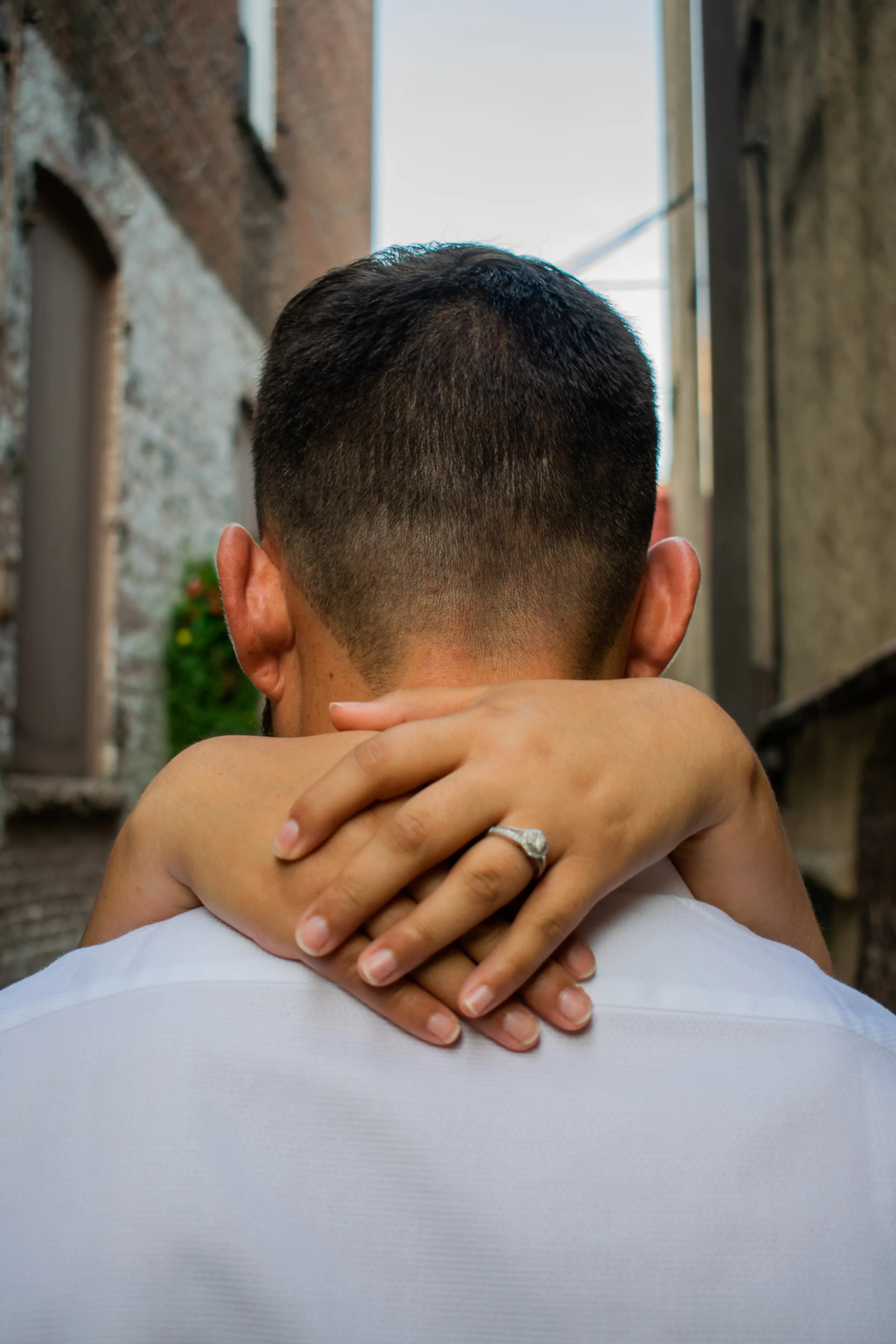 Photo from behind the groom showing the bride's arms wrapped around his neck exposing the ring.