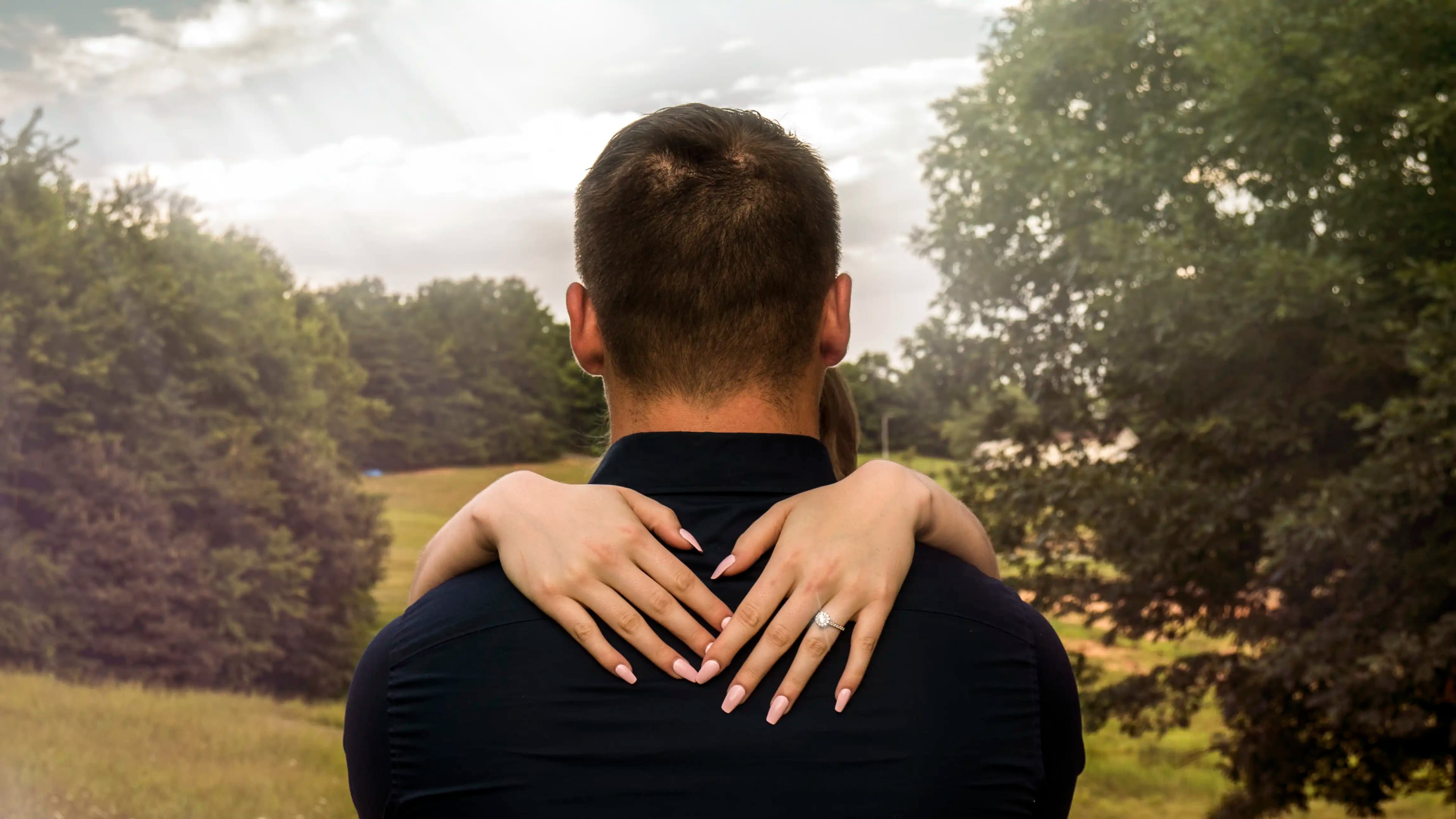 C + L embracing each other showing the back of the groom with the bride's hands around his neck exposing her ring.