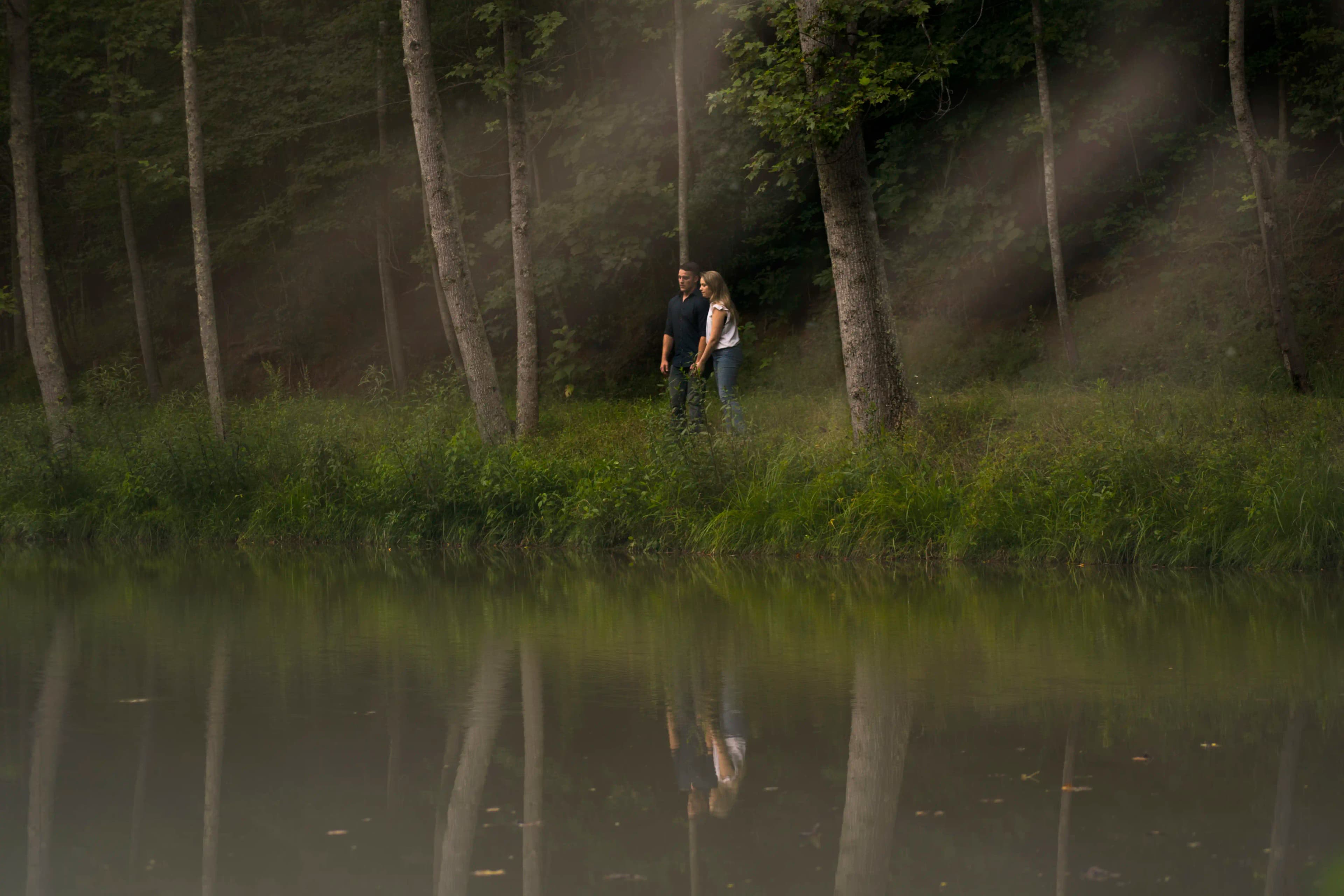 C + L walking along the bank of a pond together looking out over the water.