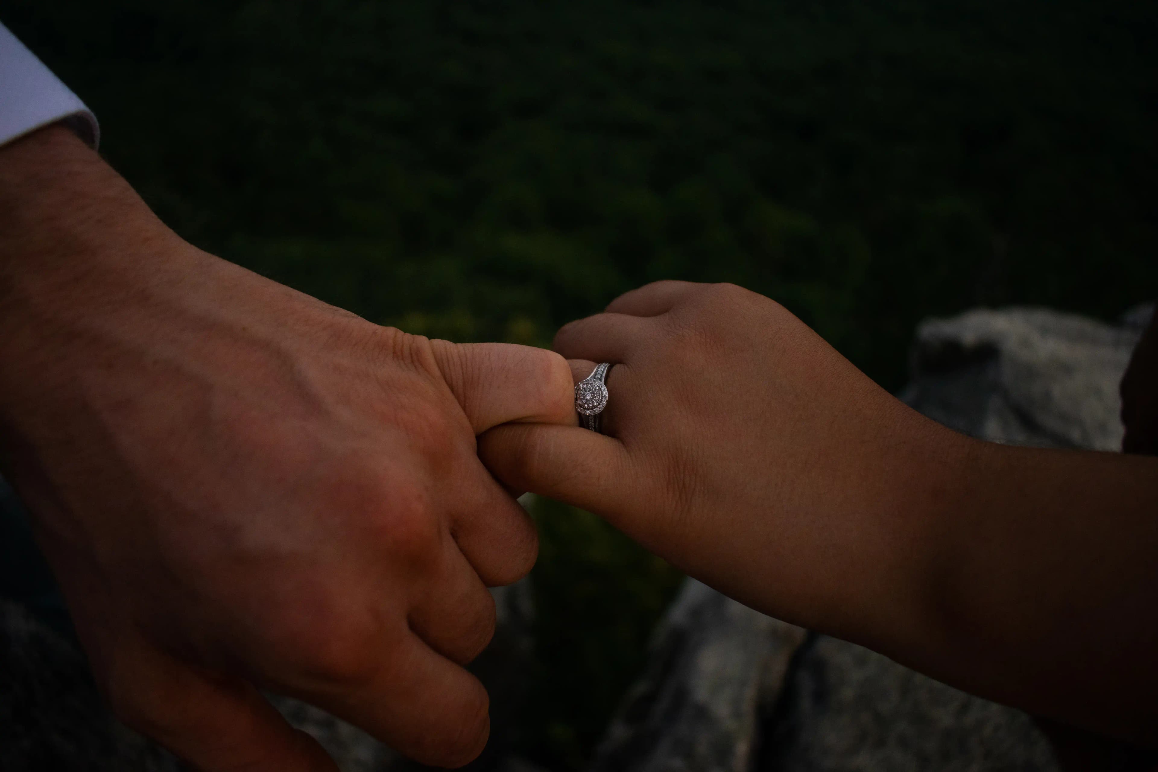 A close-up photo of D + L locking their pinkies together with the ring in view.