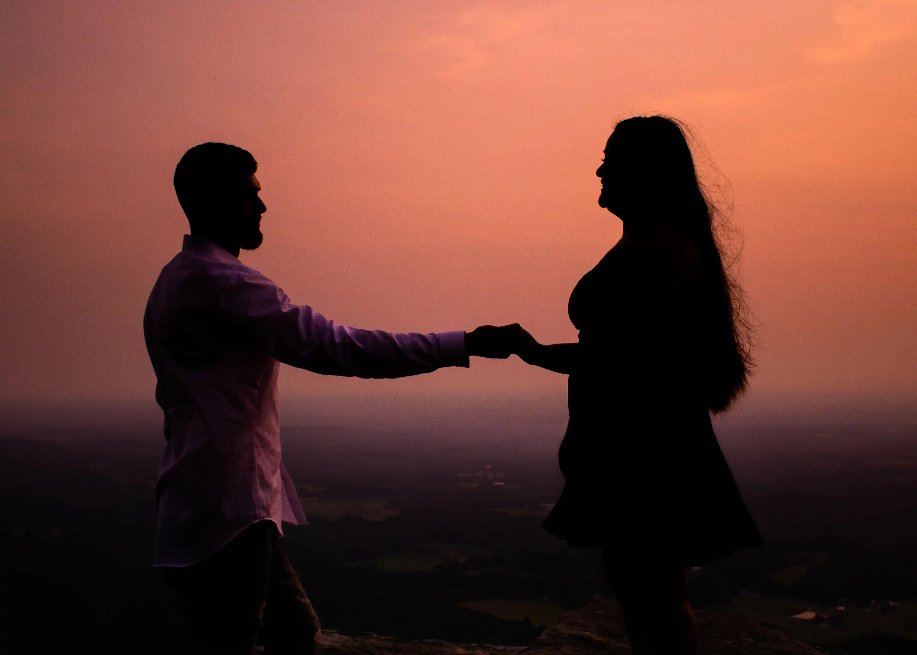 the bride & groom silhouetted by the sunset holding each others hand.