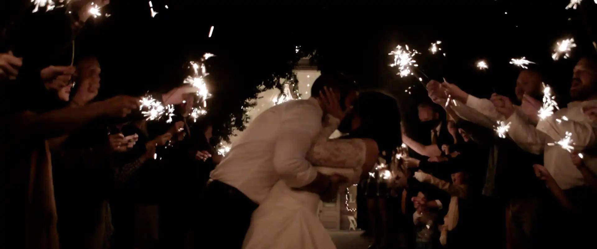 The groom dipping the bride for a kiss during the walkout surrounded by people holding sparklers.