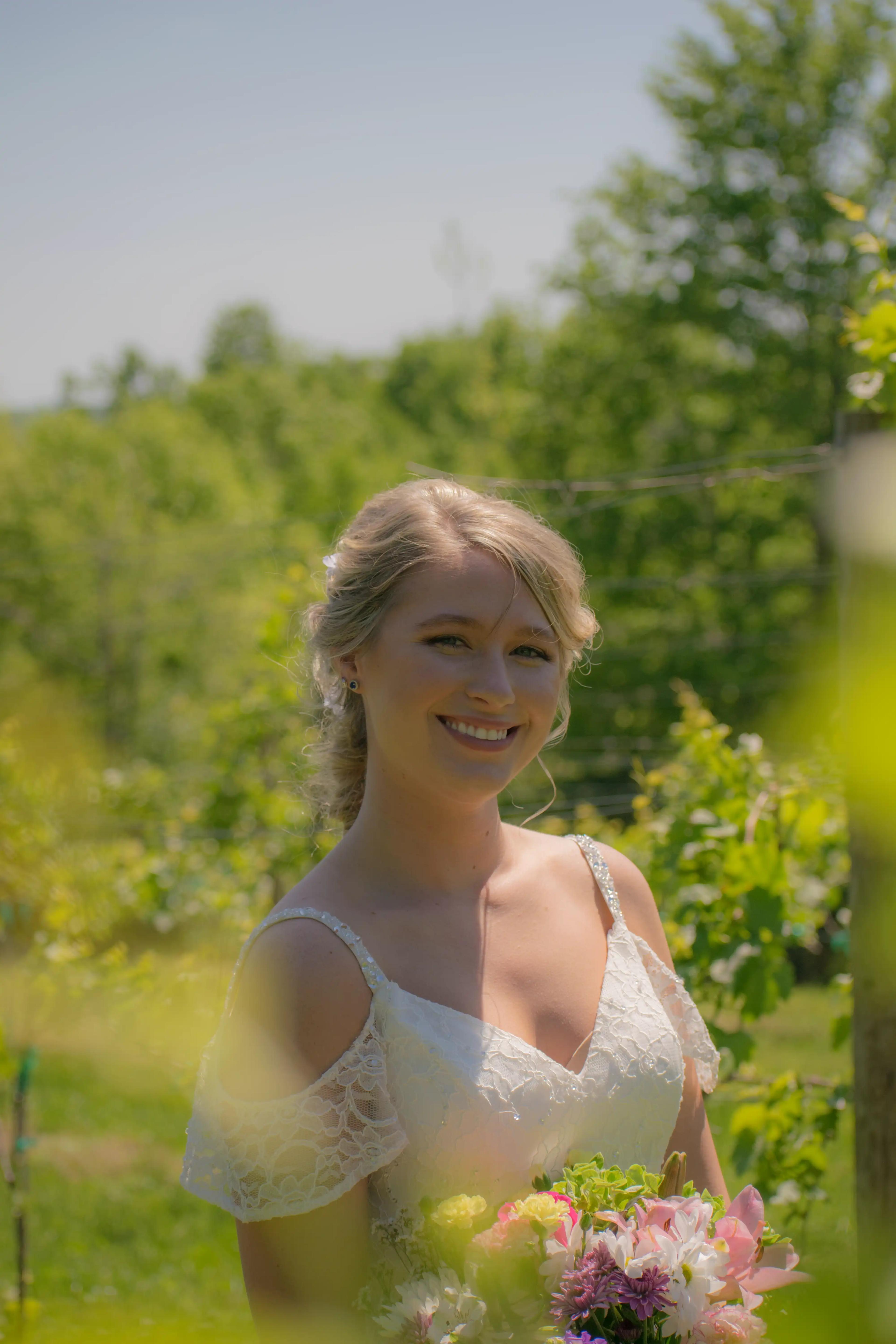 A close-up of the bride smiling in a vineyard with vines in the foreground and background drawing attention to the bride.