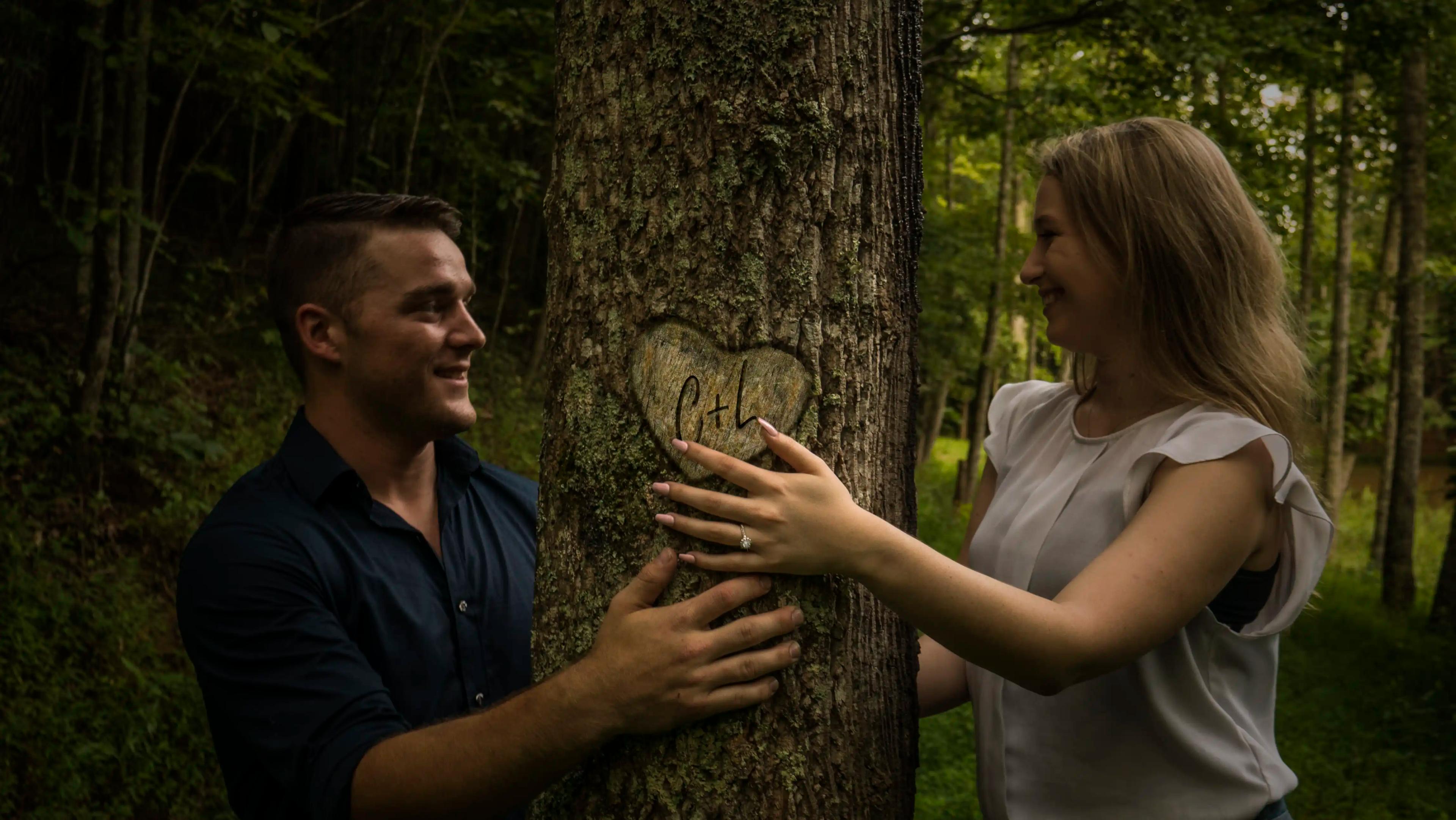 C + L smiling looking at each other with a tree between them with their initials carved into it.